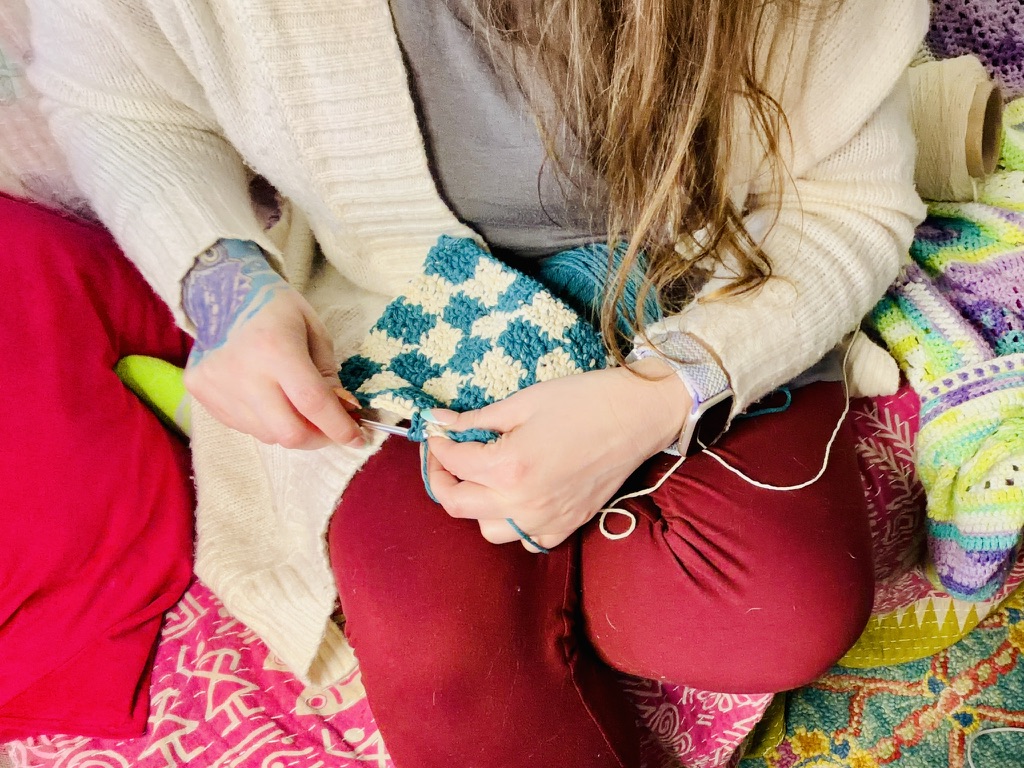 Woman with sweater crocheting a checkered dishcloth in a cozy room